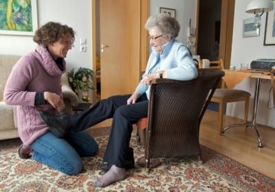 verzorgende help oude mevrouw met schoenen aandoen