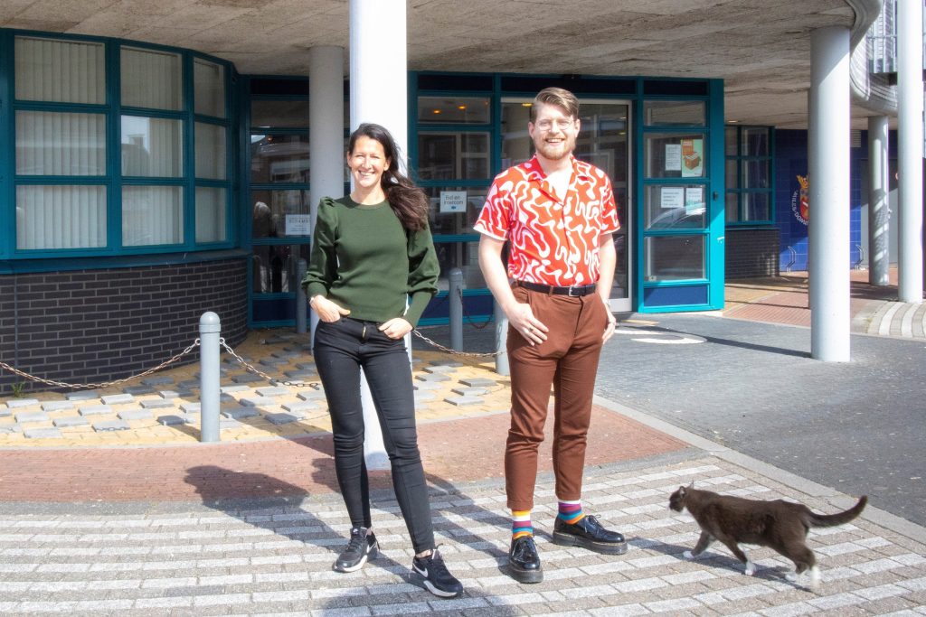 Pauline Brode en Brian Hesseling voor het gebouw in Scheemda, waar RWLP gevestigd is. Een kat loopt naar hen toe.