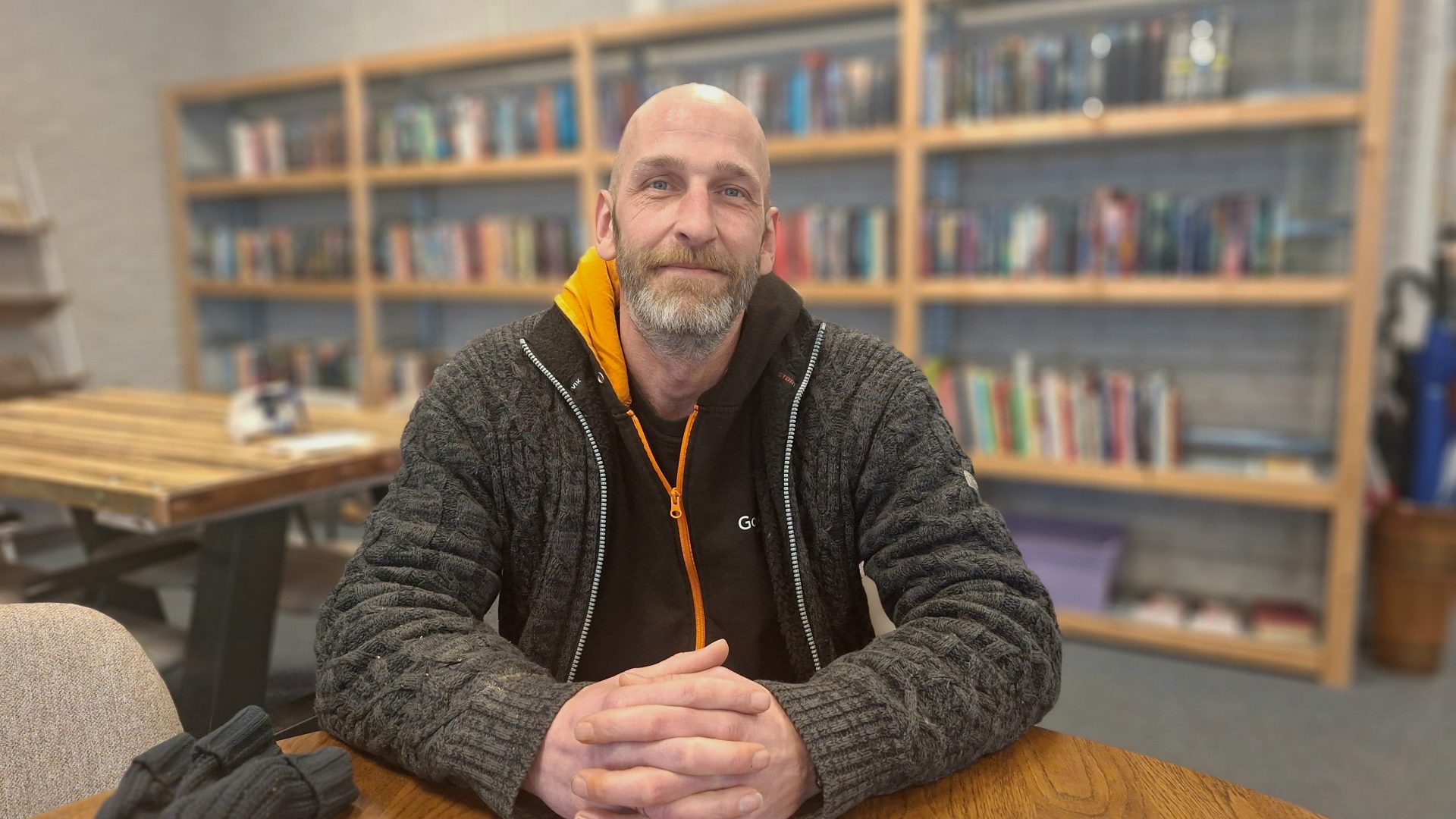 Gerrit in kringloopwinkel Goud Goed, zittend voor een kast met boeken